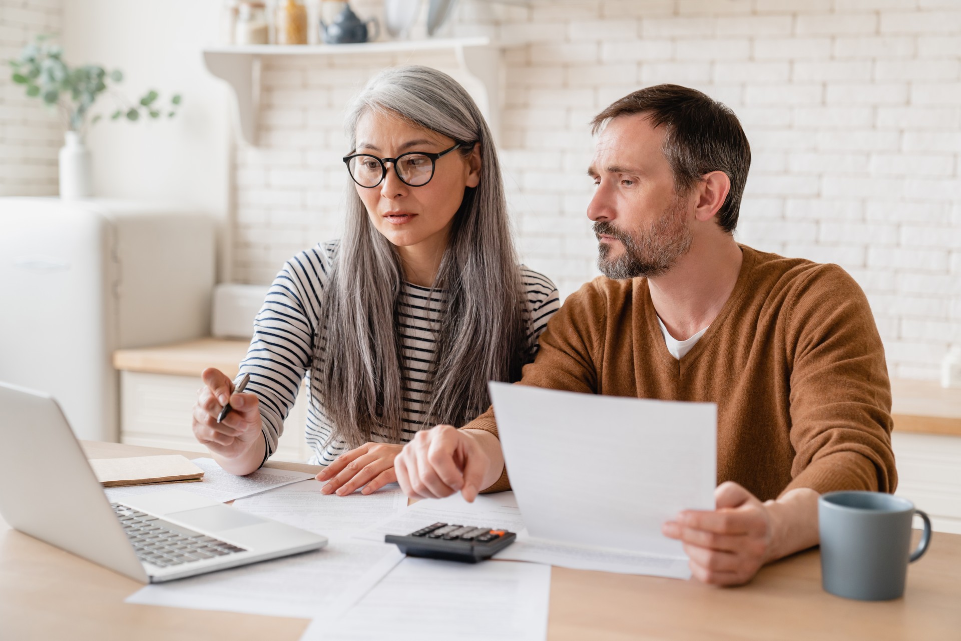 Mature middle-aged couple family wife and husband counting funds, savings declarations, investments,paperwork, financial documents, bankruptcy, court case, bills, pension with laptop.